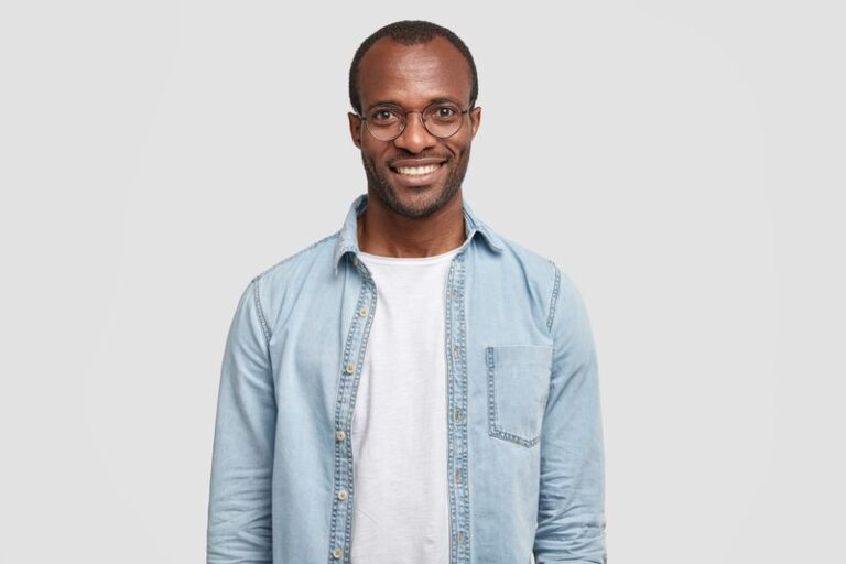 Waist up shot of handsome self confident cheerful male entrepreneur has broad smile, wears round transparent glasses, happy to meet with colleague, dressed in fashionable denim shirt isolated on white